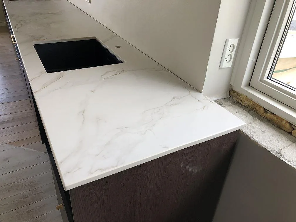 Underlimmad diskho i en matt vit Dekton Entzo köksbänkskiva med grå och guldaktig ådring, monterad vid fönster i ett kök i Kastrup.