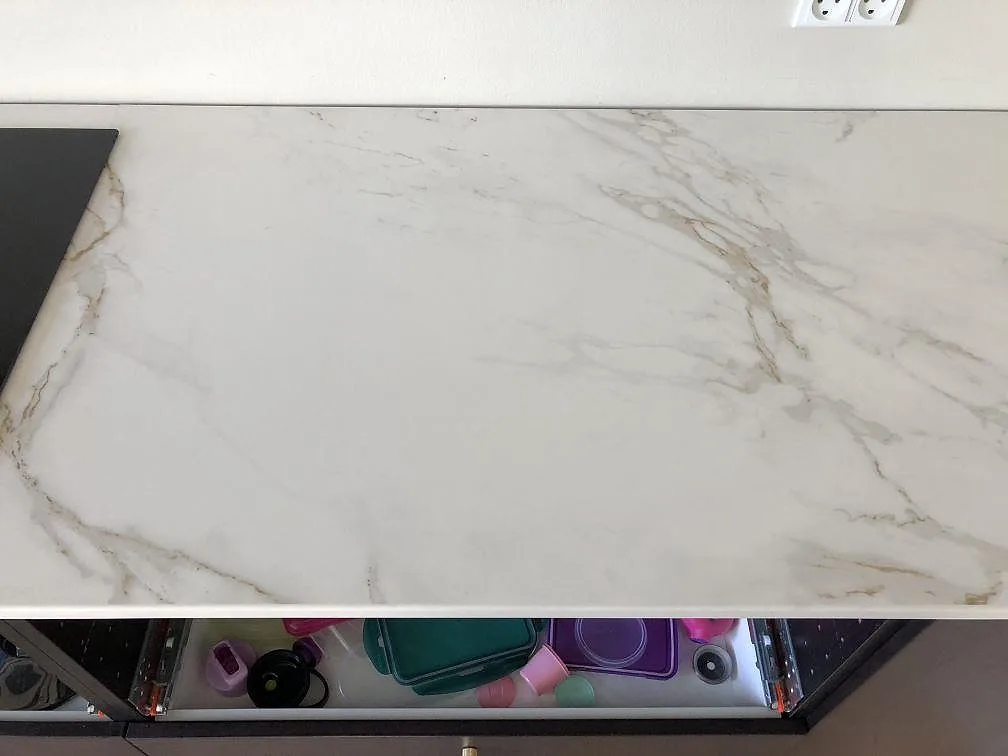 Sektion av matt vit Dekton Entzo köksbänkskiva med fin grå ådring intill induktionshällen i ett kök i Kastrup.