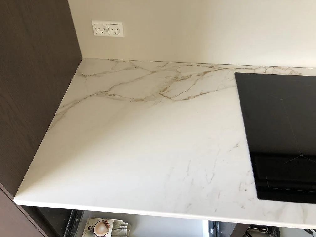 Hörn av matt vit Dekton Entzo köksbänkskiva med infälld induktionshäll och tydlig Calacatta-ådring i ett kök i Kastrup.