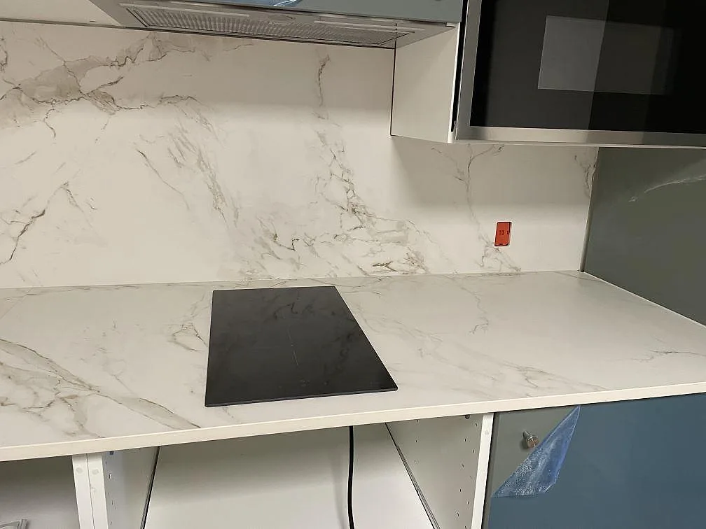 Hällsida med svart induktionshäll, matt Dekton Entzo bänkskiva och matchande väggbeklädnad i København K.