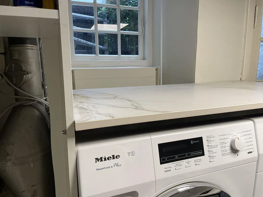 Dekton Entzo bänkskiva i matt keramik monterad över Miele tvättmaskin vid fönster i København K.
