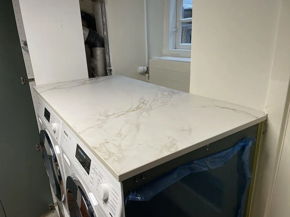 Lång arbetsyta i matt Dekton Entzo keramik över tvättmaskin och blå stomme under montering i København K.