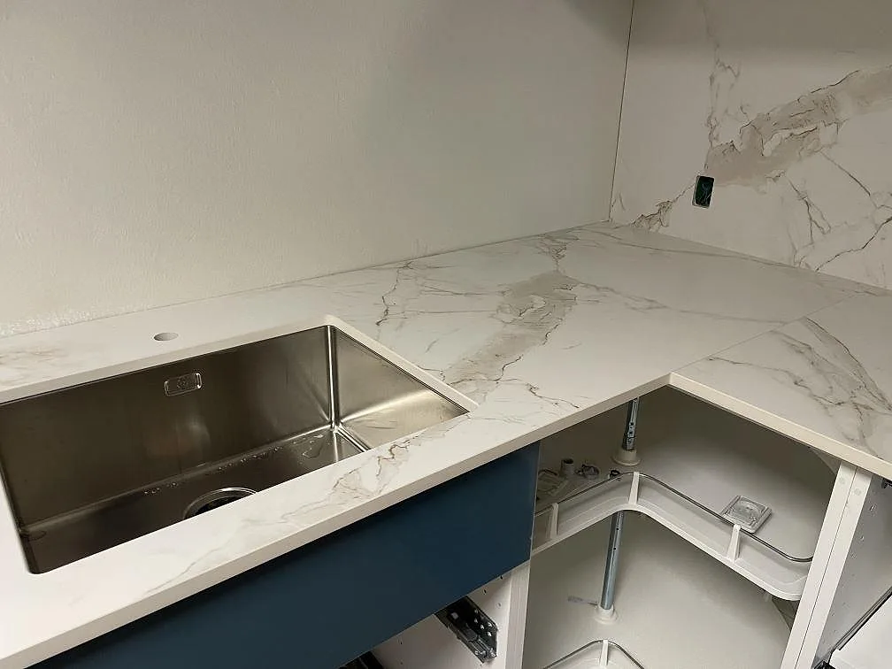 Närbild av underlimmad rostfri diskho i matt Dekton Entzo bänkskiva med vit ådring i ett kök i København K.