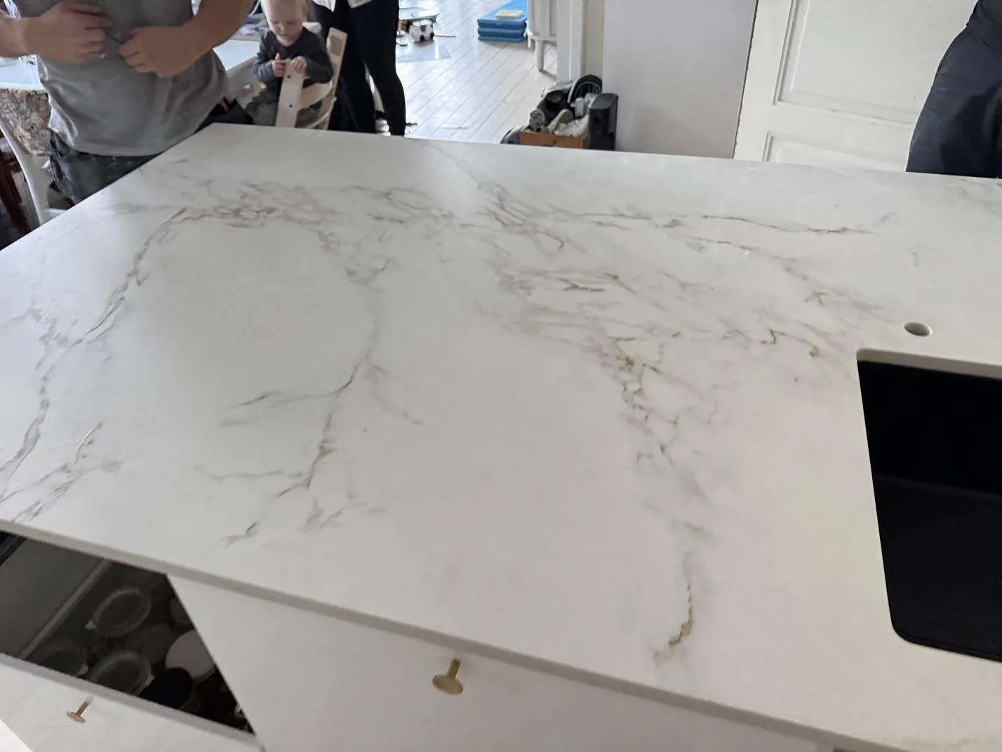 Detalj av den matta Dekton Entzo arbetsytan med ljus marmorering, svart diskho vid kanten och köket under montering i København NV.