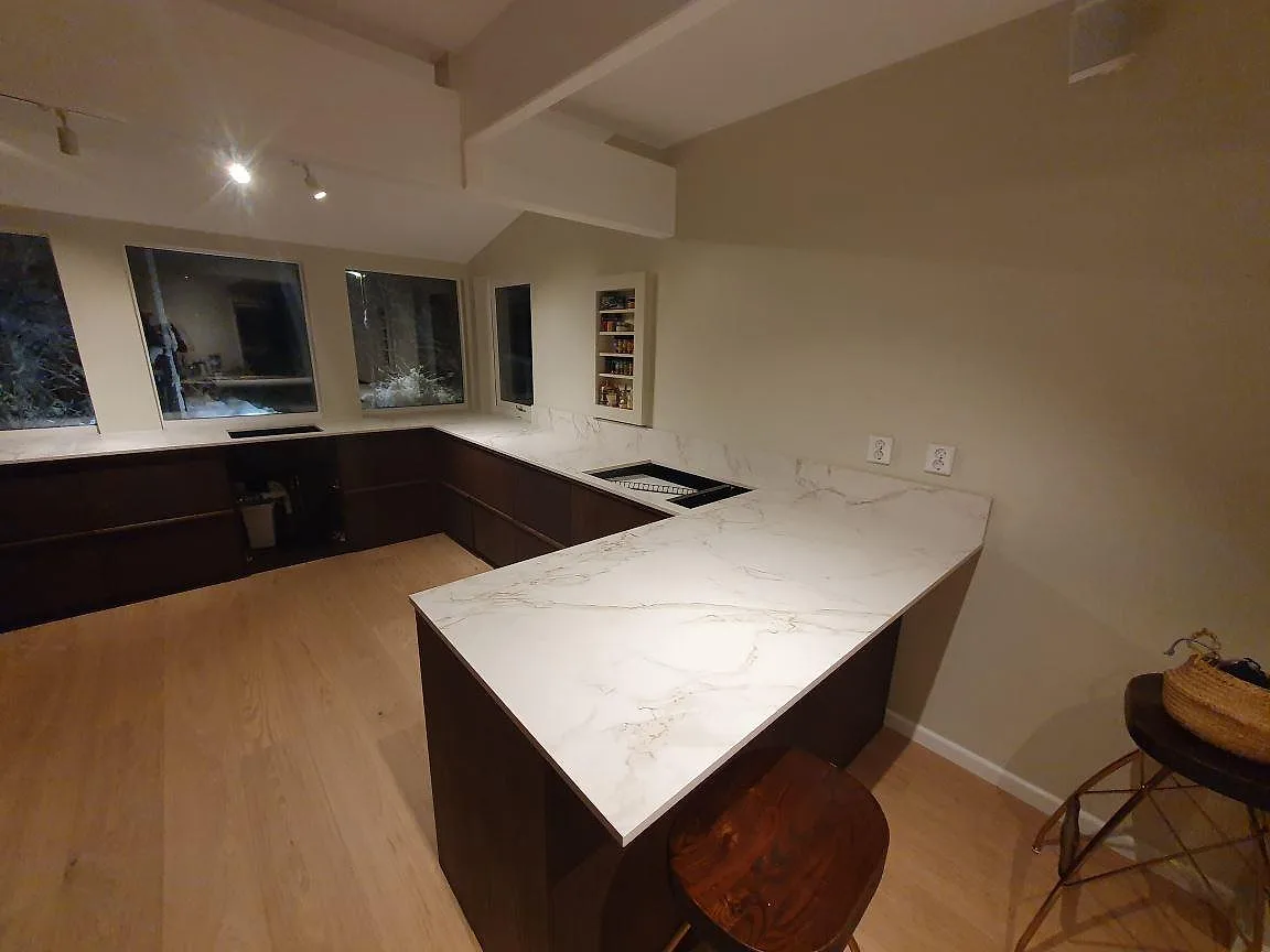 Köksbänkskiva i Dekton Entzo, ljus marmorlik keramik med grå ådring och matt yta, monterad i ett U-format kök med mörka valnötsfronter i Lidingö.