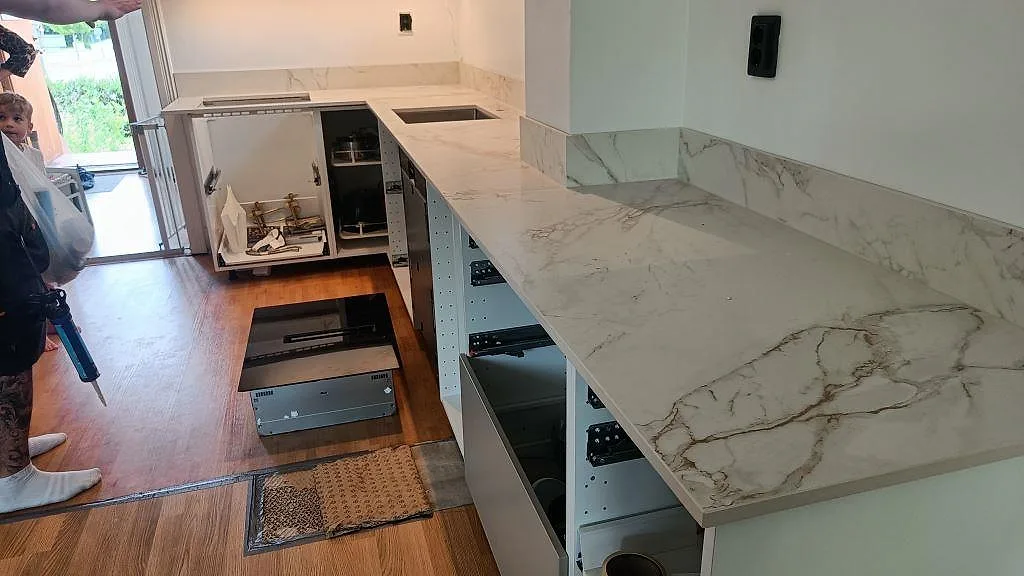 Köksbänkskiva i vit Dekton Entzo med marmorlik ådring, monterad i ett L-format kök i Malmö under installationen med öppna stommar och rostfri diskho.