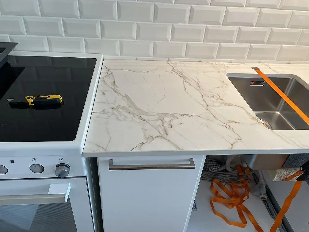 Matt köksbänkskiva i Dekton Entzo mellan svart häll och rostfri diskho i ett vitt kök i Malmö.
