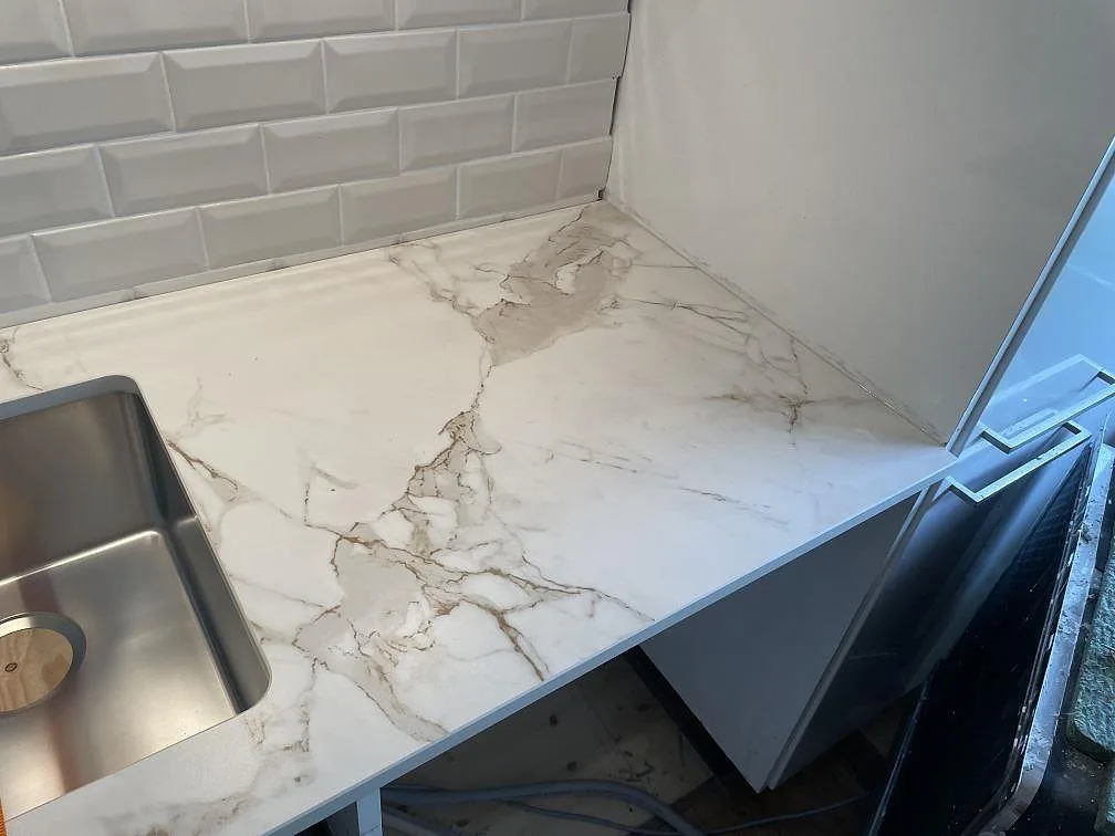 Närbild på matt Dekton Entzo bänkskiva med rostfri underlimmad diskho och vit kakelvägg i Malmö.