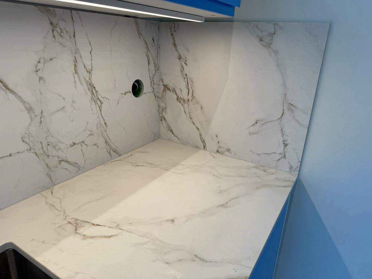 L-hörn i matt Dekton Entzo med bänkskiva och väggbeklädnad under blå överskåp i ett kök i Mölnlycke.