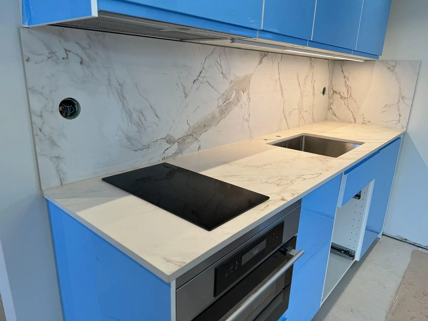 Köksbänkskiva i matt Dekton Entzo keramik med induktionshäll, underlimmad diskho och väggbeklädnad i ett blått kök i Mölnlycke.