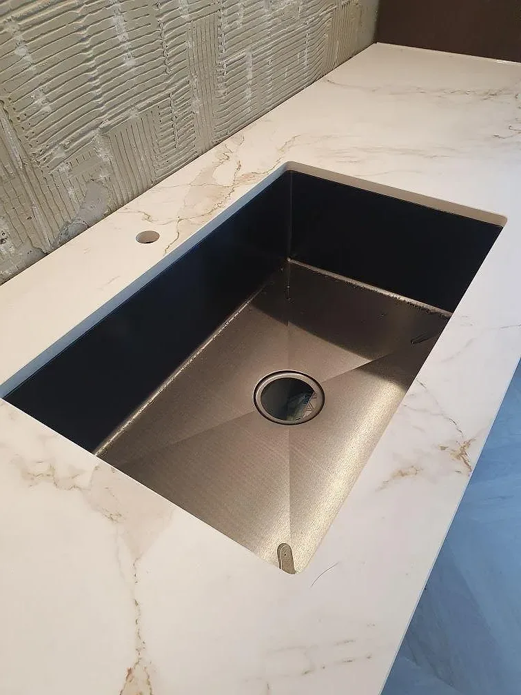 Underlimmad rostfri diskho i en bänkskiva av vit Dekton Entzo med guldådring i ett kök i Norrköping.