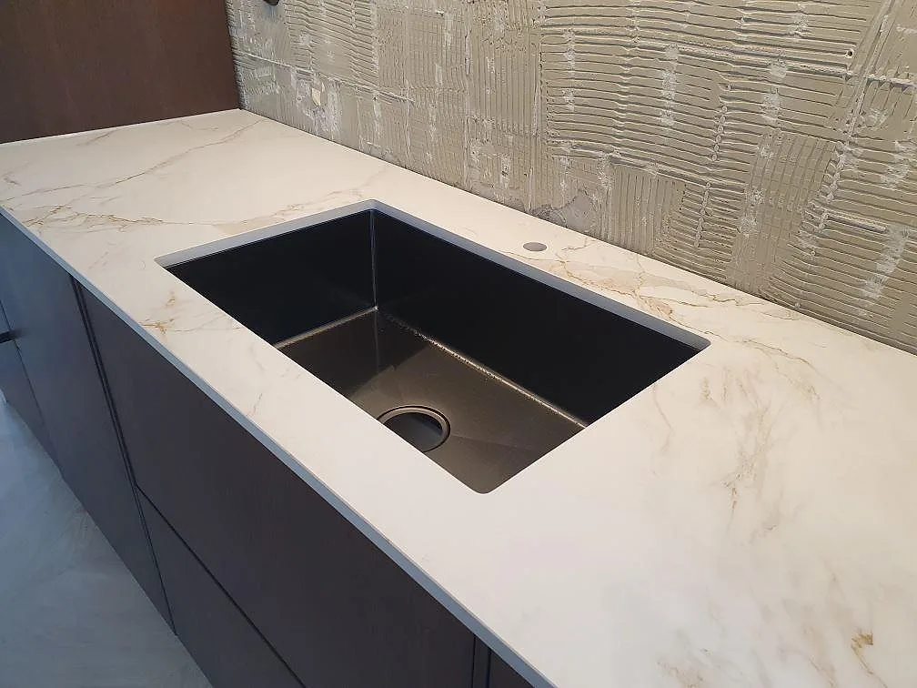 Köksbänkskiva i vit Dekton Entzo, matt, med underlimmad rostfri diskho och tydlig guldgrå ådring i ett kök i Norrköping.