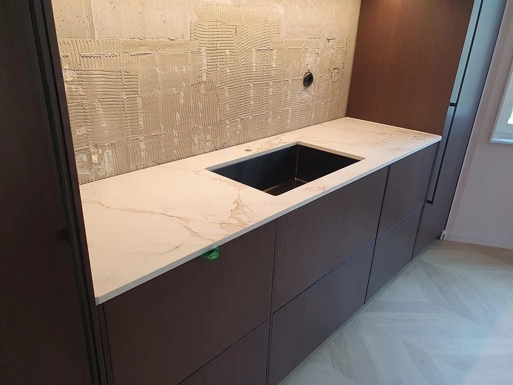 Bänkskiva i vit Dekton Entzo med underlimmad rostfri diskho och uppvikt stänkskydd i samma keramik i ett kök i Norrköping.