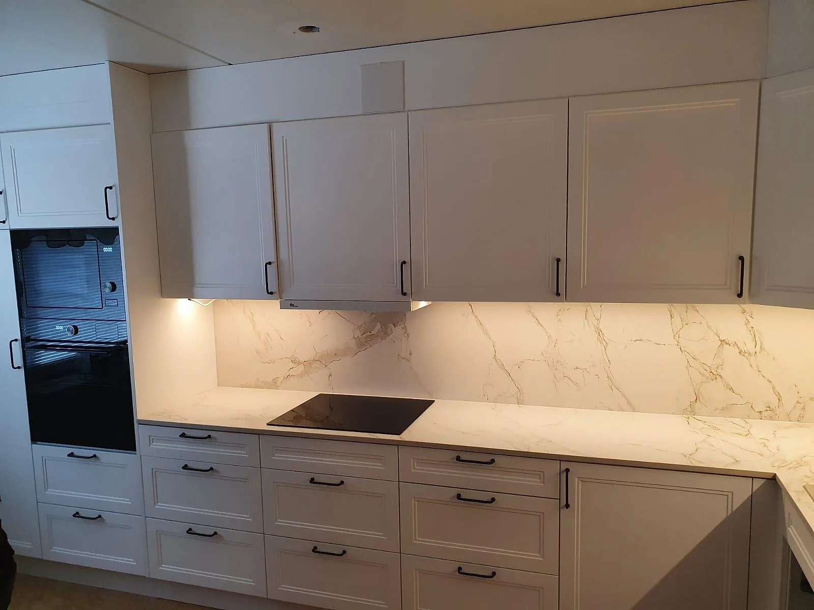 Matt köksbänkskiva i Dekton Entzo med häll och belyst marmorerat stänkskydd i ett vitt kök i Rönninge.