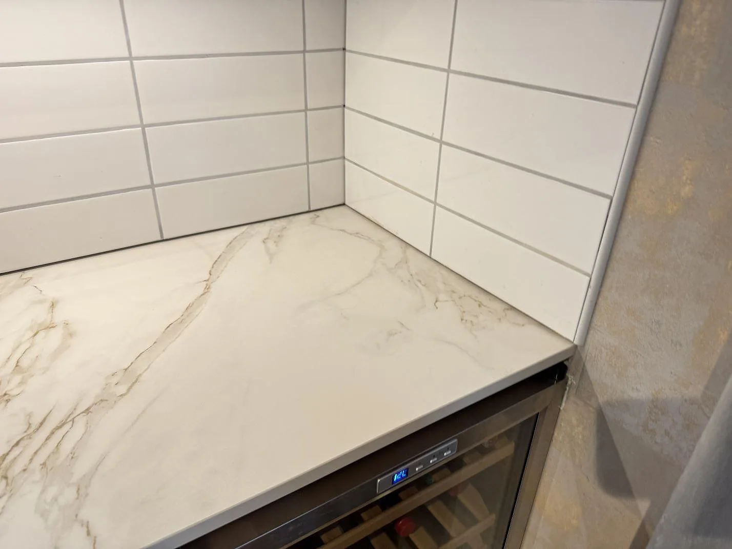 Hörnsektion av köksbänkskiva i matt Dekton Entzo, med tunn rak kant och vit kakelvägg i Sätila.