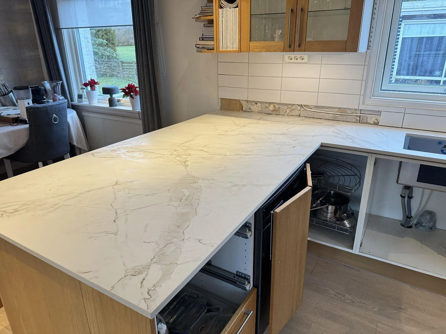 Stor köksö i matt Dekton Entzo framför väggbänken, med vit kakelvägg och träinredning i ett kök i Sätila.