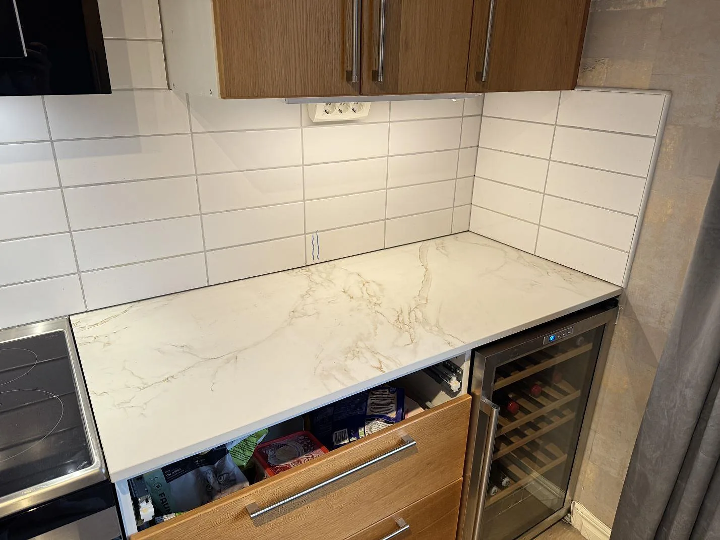 Rak väggbänk i matt Dekton Entzo mellan fristående spis och vinkyl, monterad mot vit kakelvägg i Sätila.