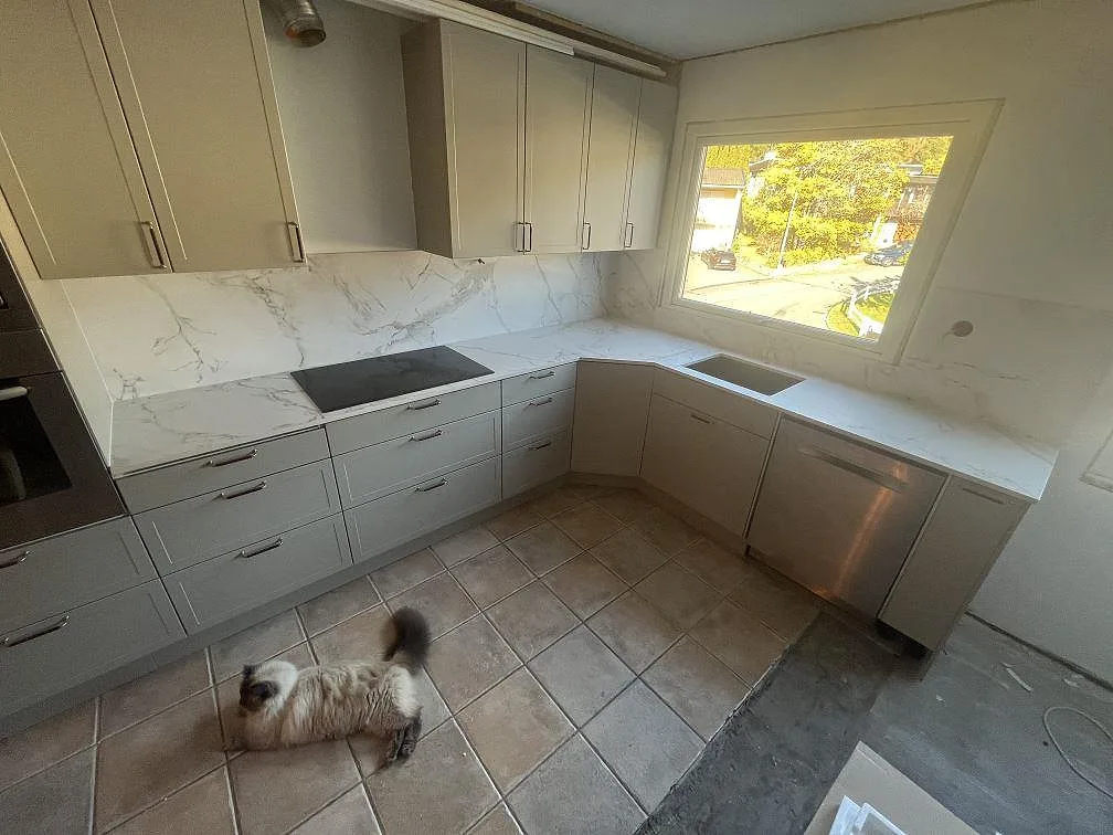 Köksbänkskiva i vit Dekton Entzo keramik, matt yta, med induktionshäll, diskholäge och matchande stänkskydd i ett U-format kök i Saltsjö Boo.
