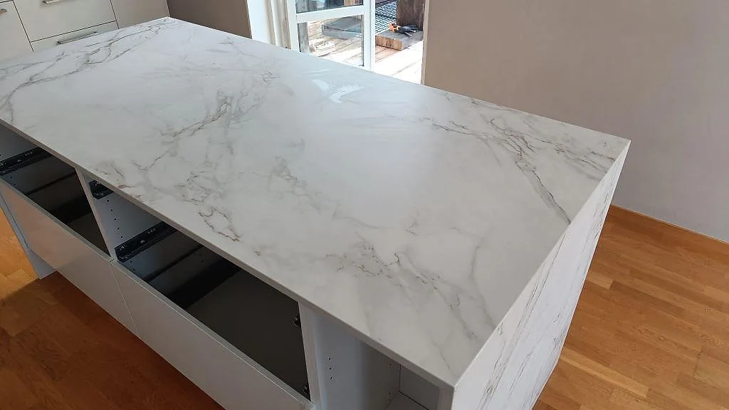 Närbild uppifrån på den matta Dekton Entzo köksbänkskivan med ljus Calacatta-lik ådring och öppna stommar under montering i Staffanstorp.