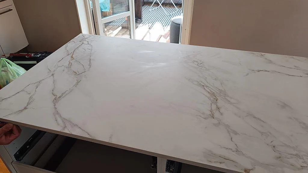 Detalj av den matta Dekton Entzo-ytan på köksön, vit keramik med grå och varma ådringar under montering i Staffanstorp.