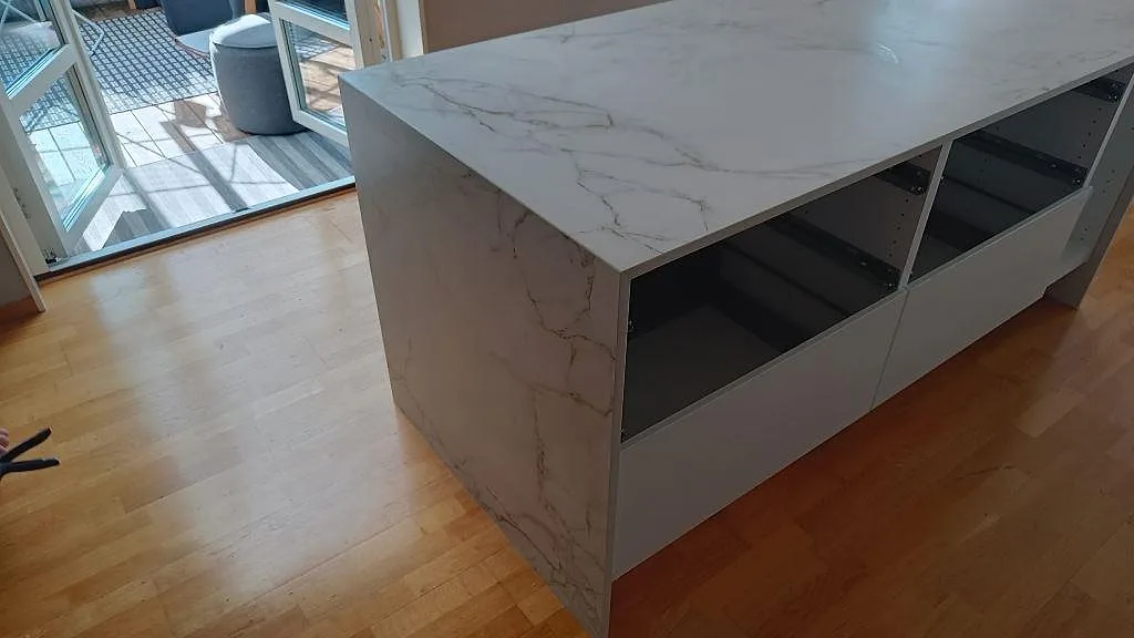 Köksö i matt Dekton Entzo med klädd gavel och öppna skåpstommar, fotograferad vid altandörr i ett kök i Staffanstorp.