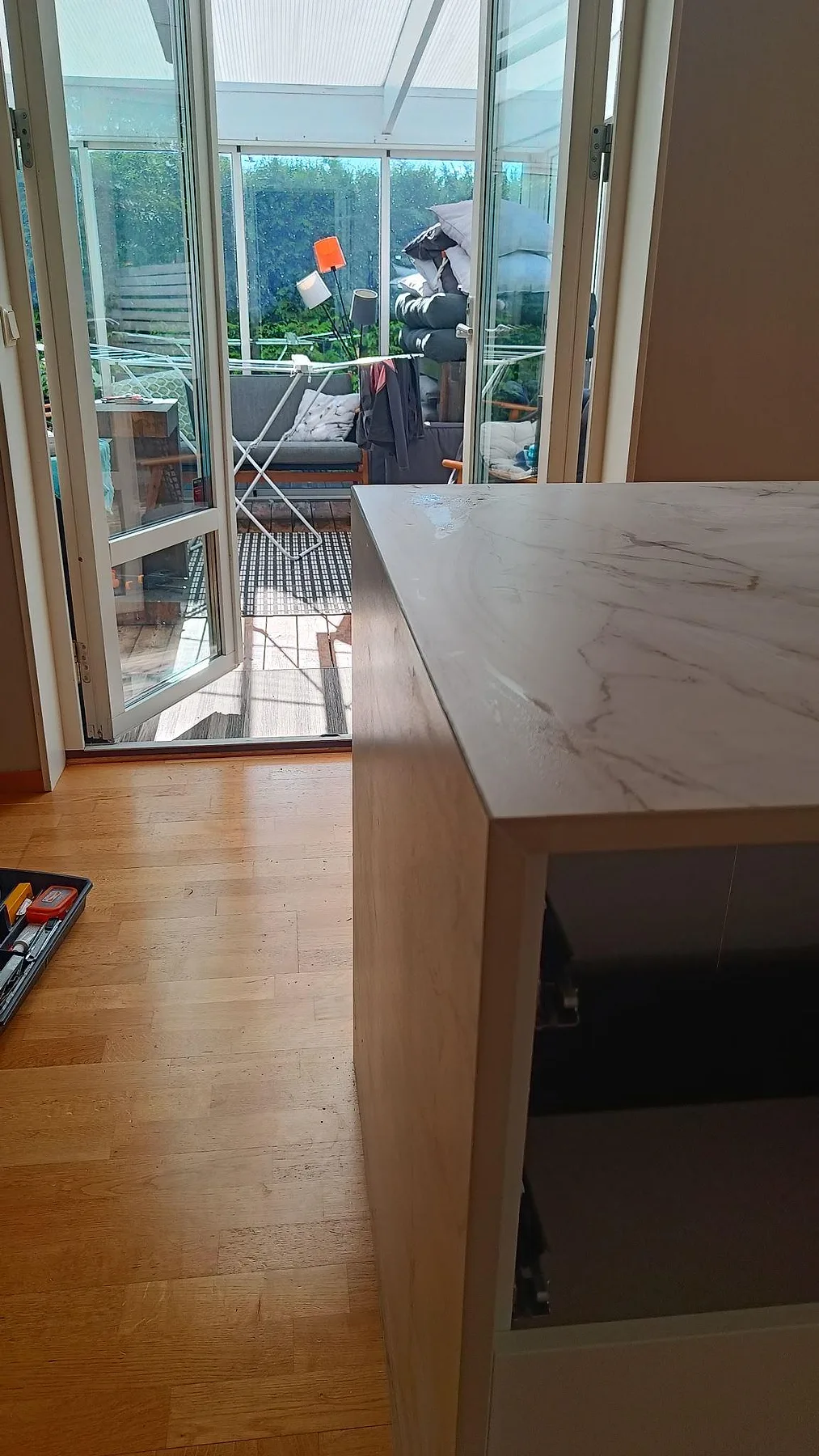 Hörnvy av köksö i matt Dekton Entzo intill altandörr, med ljus bänkskiva och ådrad gavel i Staffanstorp.