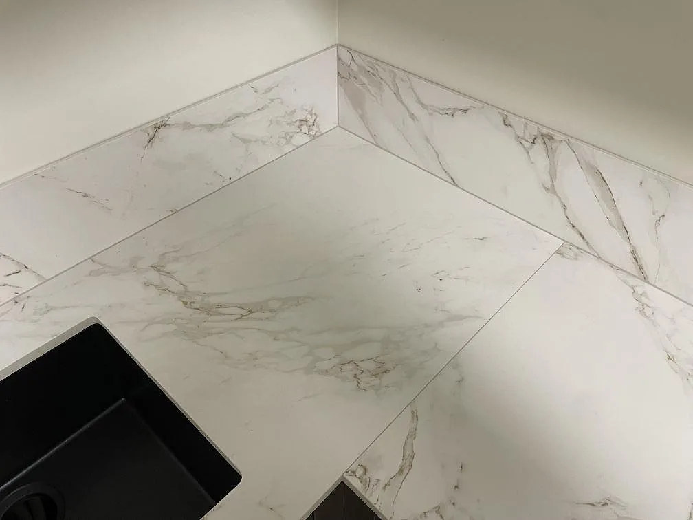 Detalj av hörnet i matt Dekton Entzo keramik med 8 mm stänkskydd och grå ådring vid diskhon i ett kök i Stockholm.