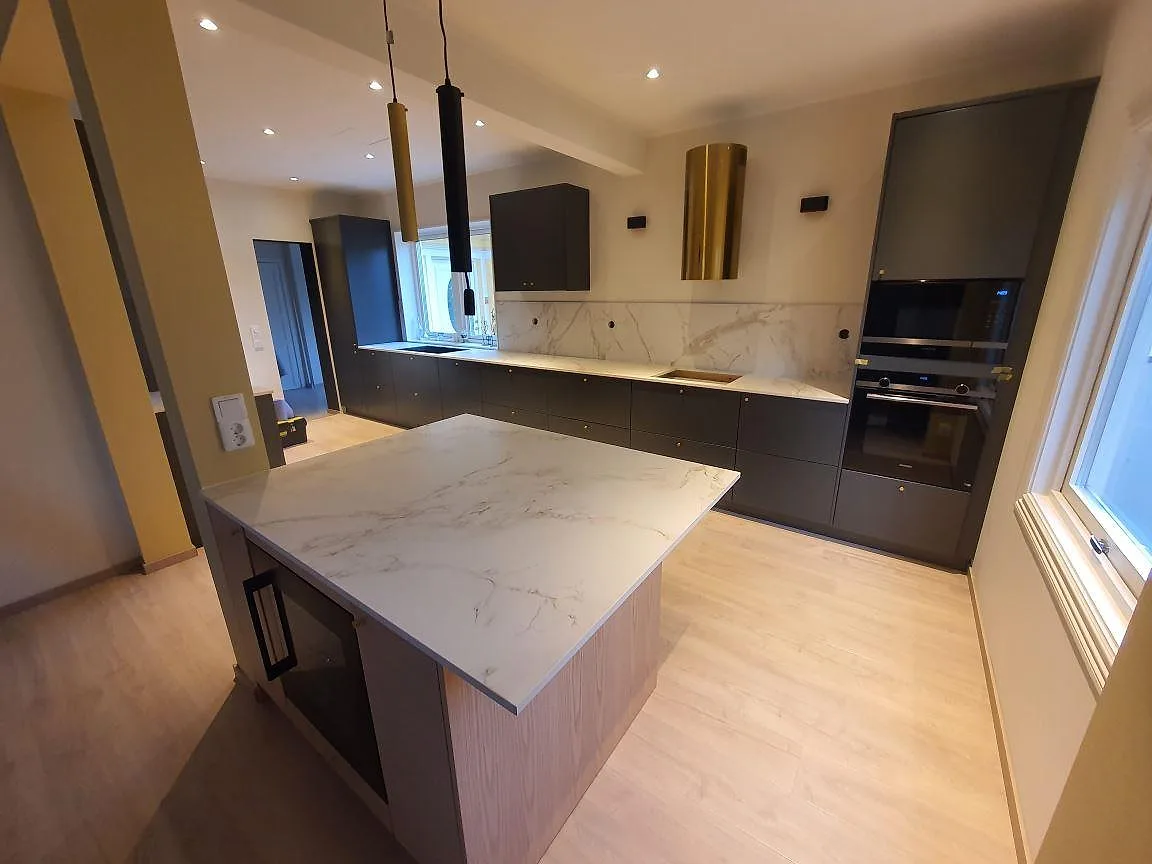 Köksbänkskiva och köksö i vit Dekton Entzo Matt med marmorerad ådring och stänkskydd i ett kök i Sundbyberg.