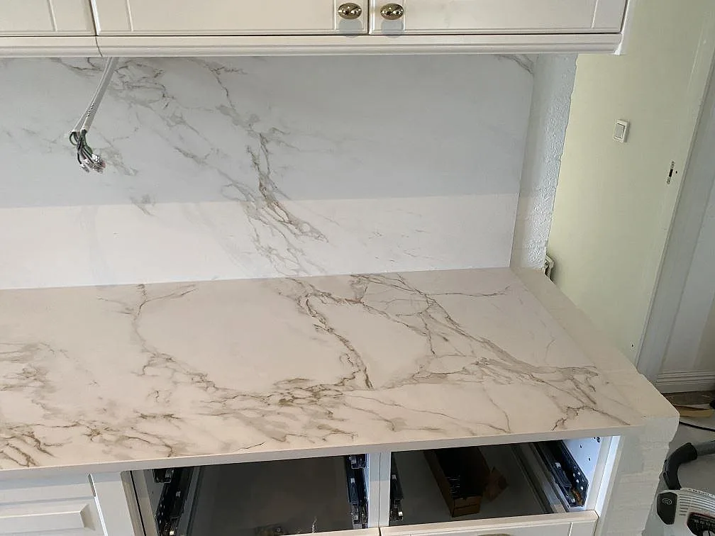 Bänkskiva i matt vit Dekton Entzo med grå ådring och heltäckande stänkvägg, fotad under montering i ett kök i Svedala.