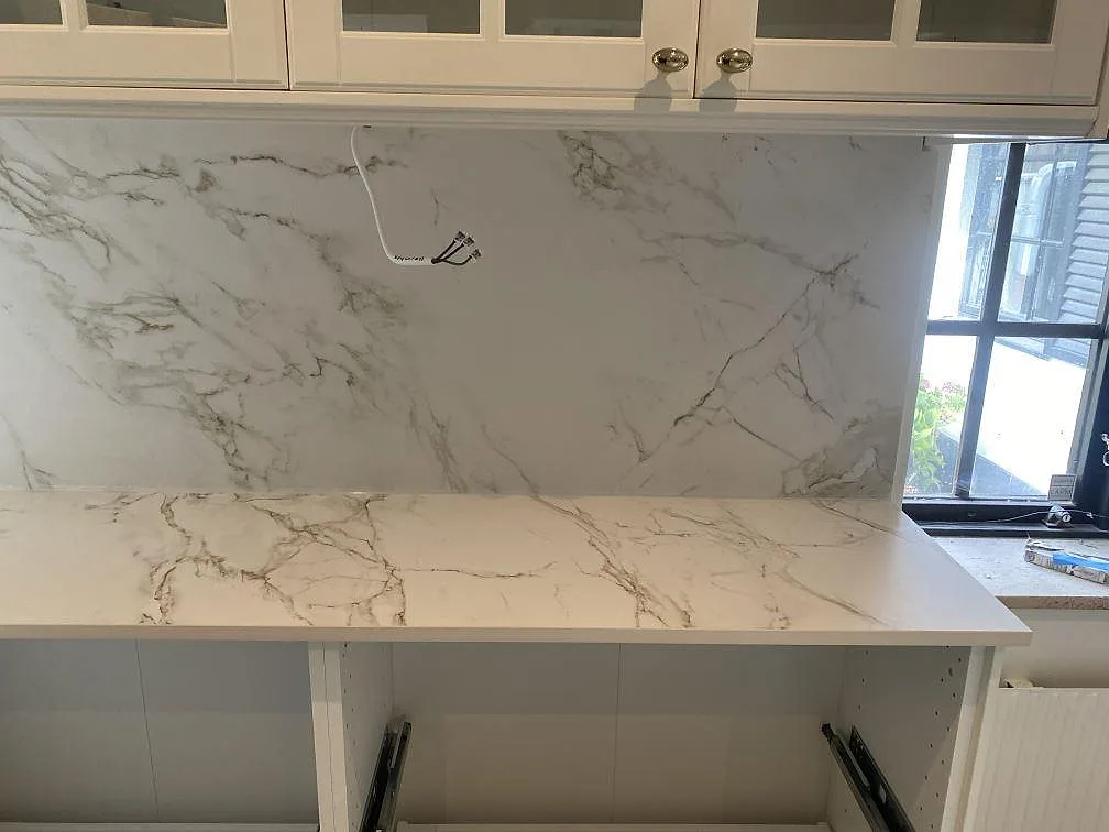 Bänkskiva i vit Dekton Entzo, matt, med heltäckande stänkvägg i samma sten vid ett köksfönster i Svedala.