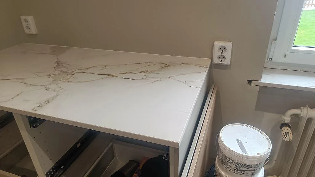 Detalj av väggbänk i matt Dekton Entzo med grå ådring intill fönster och köksstommar i Trelleborg.
