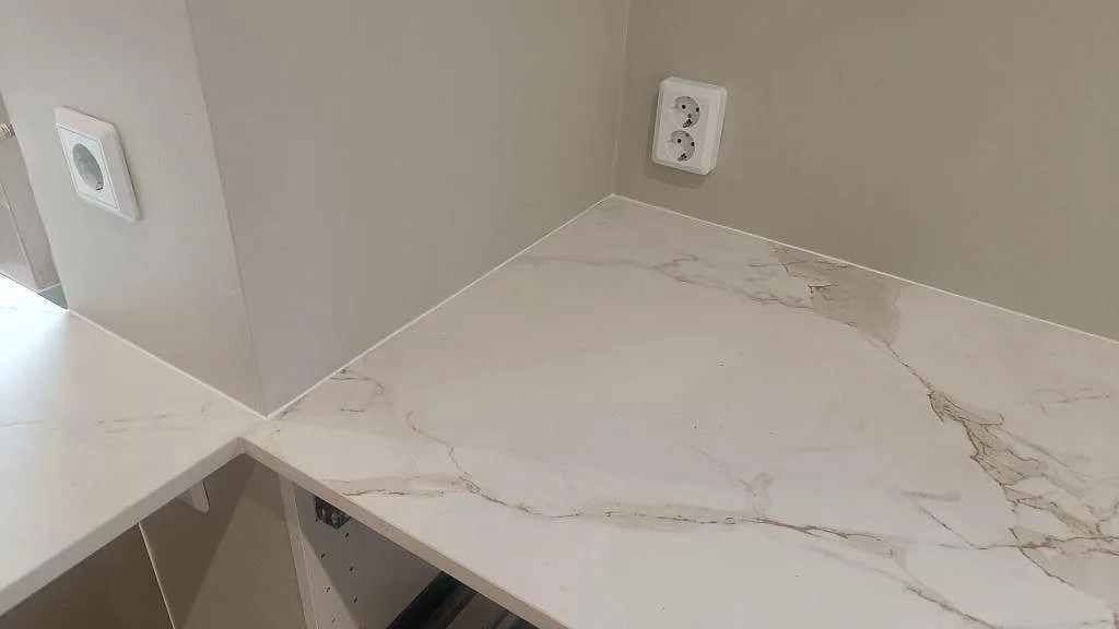 Hörnpassning mellan köksö och väggbänk i matt Dekton Entzo med ljus marmorerad yta i Trelleborg.