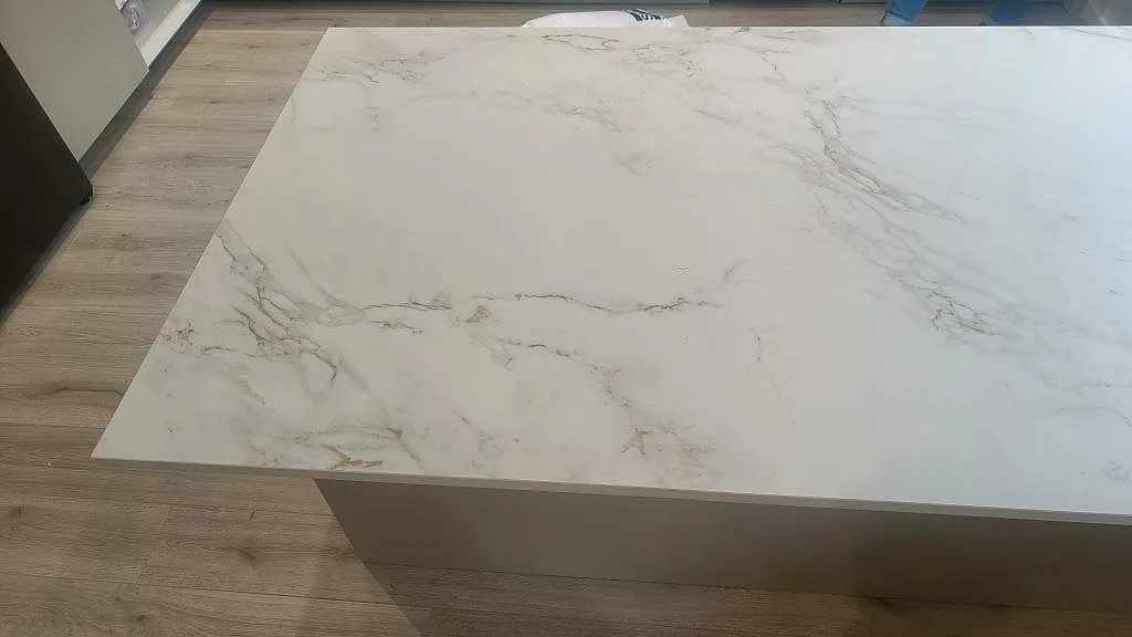 Närbild av köksö i matt Dekton Entzo, vit keramik med grå ådring och rak framkant i ett kök i Trelleborg.