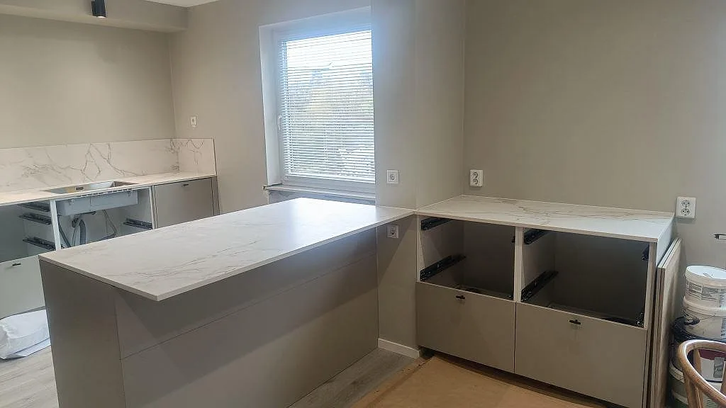 Köksbänkskiva i matt Dekton Entzo med vit marmorkänsla, grå ådring och köksö under montering i Trelleborg.