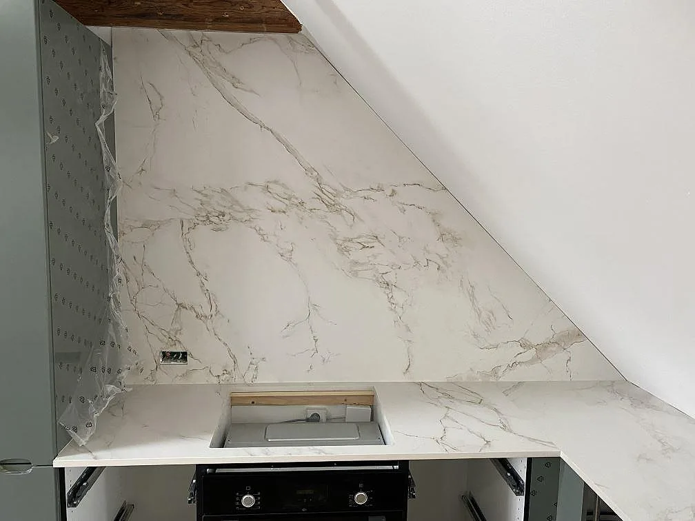 Matchande väggbeklädnad och bänkskiva i matt Dekton Entzo keramik bakom hällplatsen i ett kök i Valby.