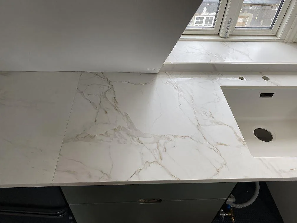 Matt Dekton Entzo bänkskiva i keramik vid diskho och fönsterparti i ett kök under montering i Valby.