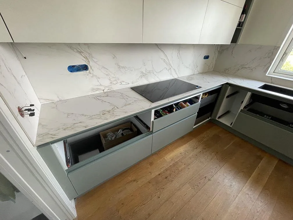 Köksbänkskiva i matt Dekton Entzo keramik med matchande väggbeklädnad och mörk hällzon i ett kök i Vendelsö.