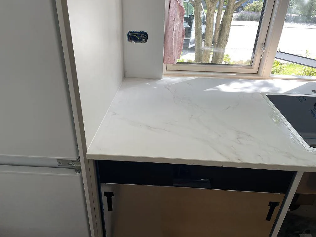 Köksbänkskiva i matt Dekton Entzo vid fönster med rostfri diskho, vit inredning och mjuk grå ådring i Virum.