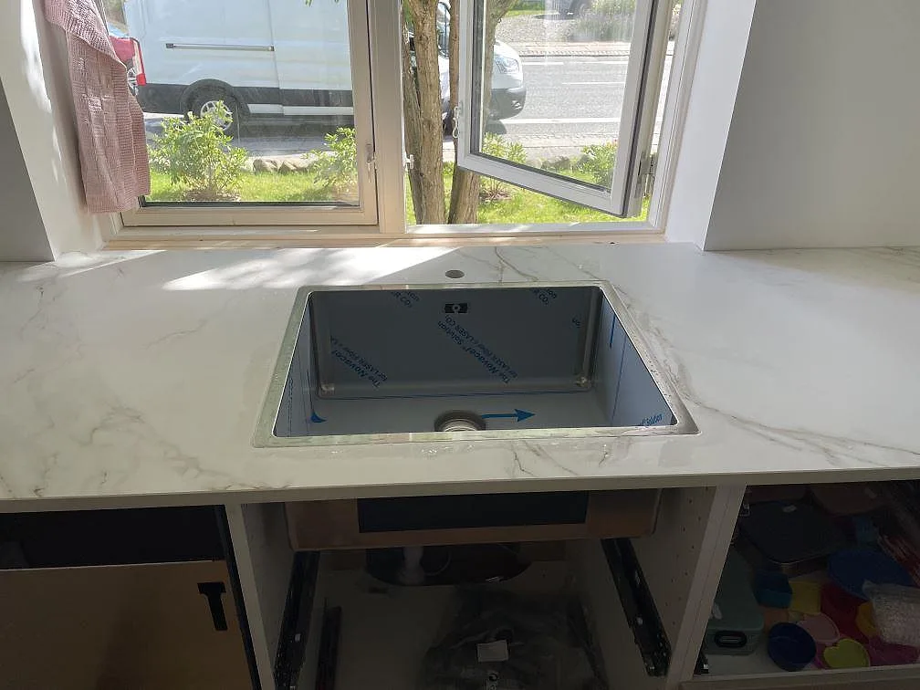 Underlimmad rostfri diskho i bänkskiva av matt Dekton Entzo keramik framför stora fönster i Virum.
