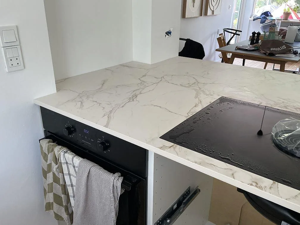 Bänkskiva i matt Dekton Entzo med svart induktionshäll, vit stenådring och kök under montering i Virum.