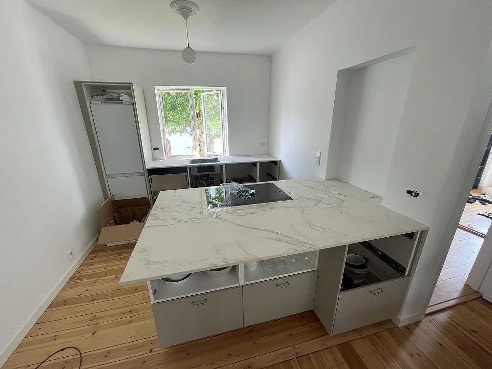 Stor köksö med bänkskiva i matt Dekton Entzo keramik, svart induktionshäll och bänkrad vid fönster i Virum.