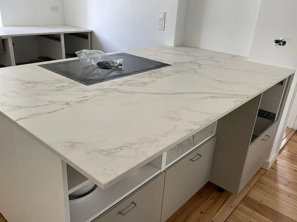Bred köksö i Dekton Entzo keramik, matt, med svart häll och ljus ådring över vit köksinredning i Virum.