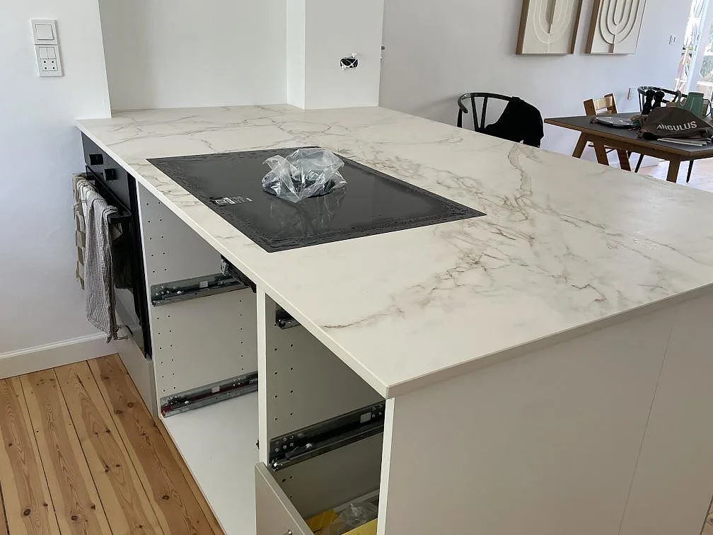 Närbild på köksö i matt Dekton Entzo keramik med svart induktionshäll, vit Calacatta-look och öppna stommar i Virum.