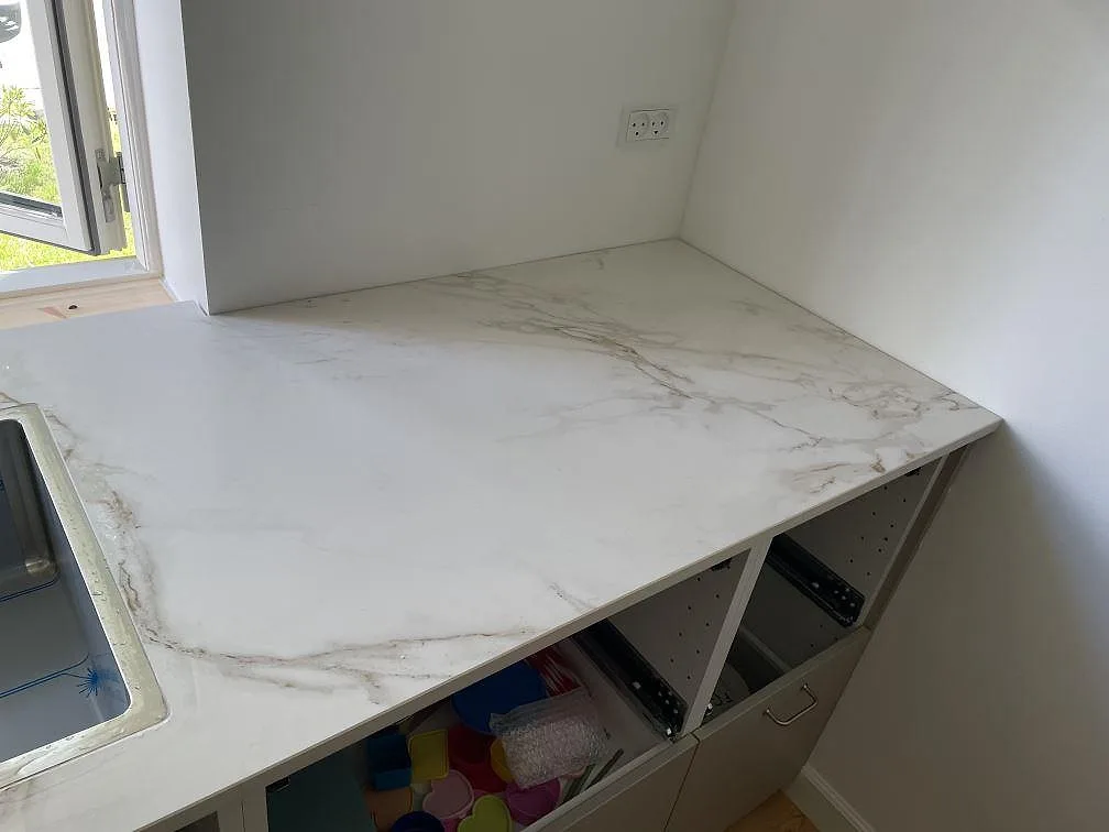 Bänkrad i matt Dekton Entzo keramik med underlimmad rostfri diskho, ljus ådring och öppna skåpstommar i Virum.