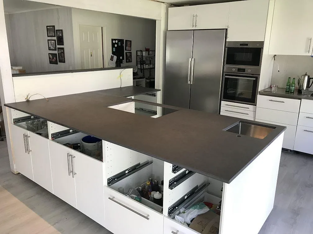 Köksbänkskiva i mörk Dekton Eter, Mocka, installerad på vita köksstommar i ett kök i Karlshamn.