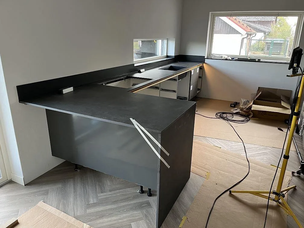 Köksbänkskiva i mörk matt Dekton Eter med köksö, väggbänkar och stänkskydd i ett kök i Vankiva.