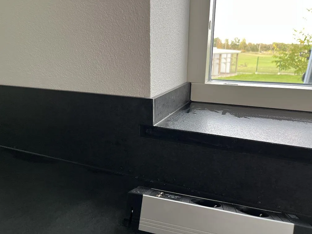 Mörk fönsterbänk och stänkskydd i matt Dekton Eter monterade runt köksfönster i Vankiva.