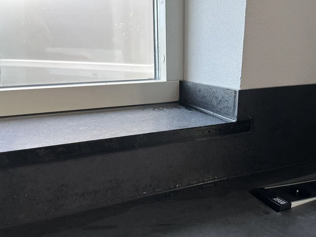 Detalj av fönsterbänk och uppvikt stänkskydd i mörk matt Dekton Eter vid köksfönster i Vankiva.