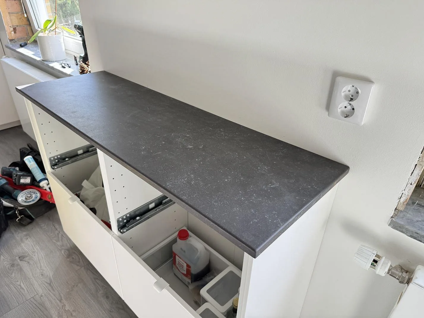 Lång köksbänkskiva i matt Dekton Fossil keramik vid fönster och vit vägg i kök under montering i Arlöv.