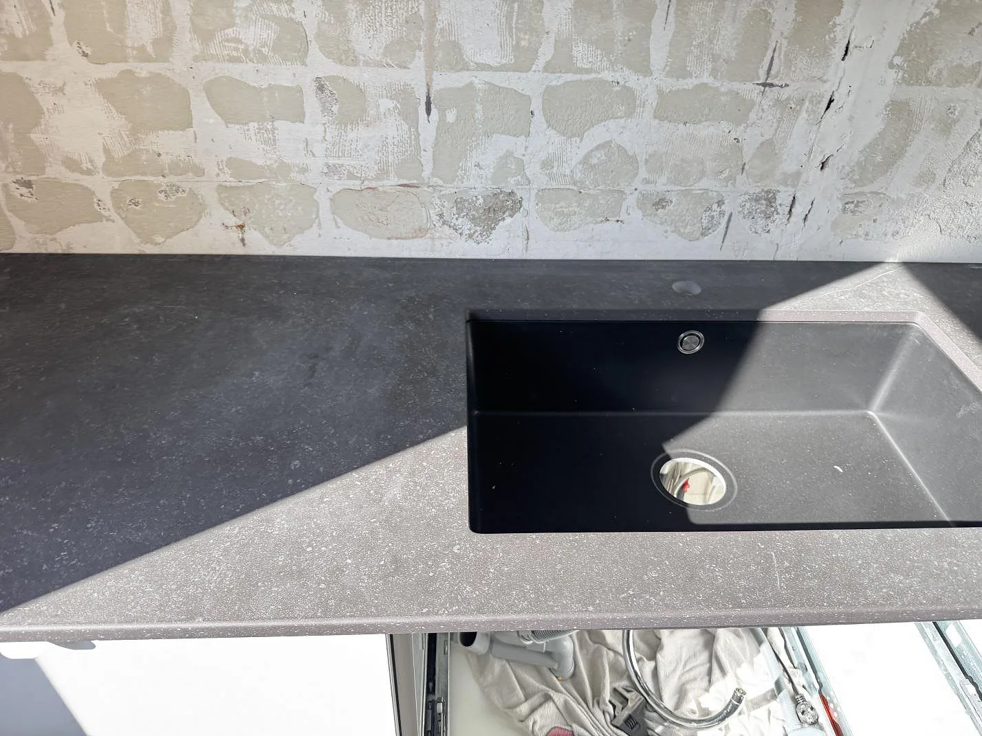 Köksbänkskiva i matt Dekton Fossil keramik med svart diskho och bar vägg under montering i Arlöv.